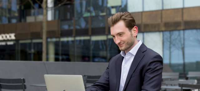 Ein junger Geschäftsmann arbeitet im Freien am Laptop und plant die Finanzierung seines MBA.