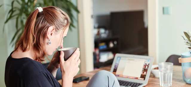 Eine Frau sitzt mit Kaffee am Schreibtisch und recherchiert am Laptop die Kosten eines MBA.