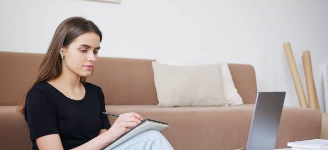 Eine Studentin macht sich mit Kopfhörern Notizen neben ihrem Laptop, etwa bei der Bewerbung um ein MBA-Stipendium.