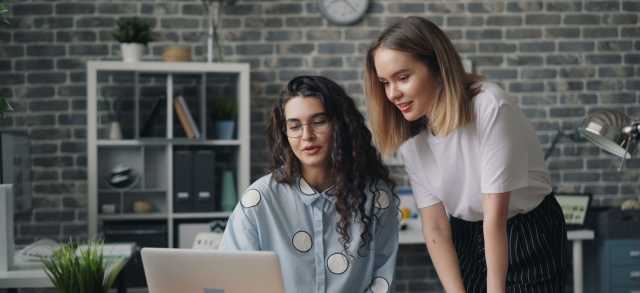 Junge Berufseinsteigerinnen mit Abitur besprechen ein Projekt am Laptop.