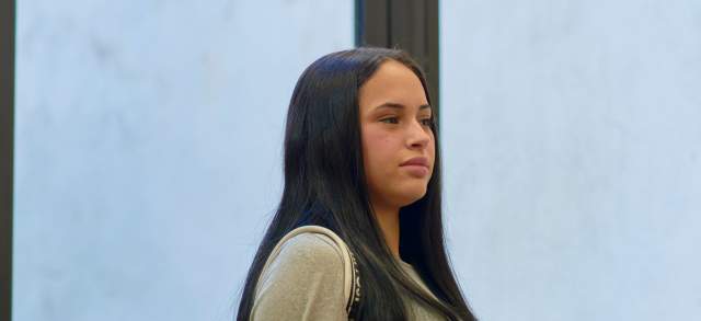 Eine junge Frau steht mit Rucksack und Büchern im Arm, bereit für die Einschreibung ins duale Studium.