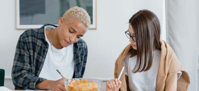 Zwei junge Leute lernen gemeinsam am Tisch und bereiten sich auf den Einstellungstest fürs duale Studium vor.