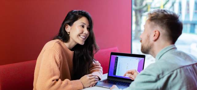 Eine junge Frau und ein junger Mann sitzen mit Laptop im Café und sprechen über Kurzarbeit im dualen Studium.