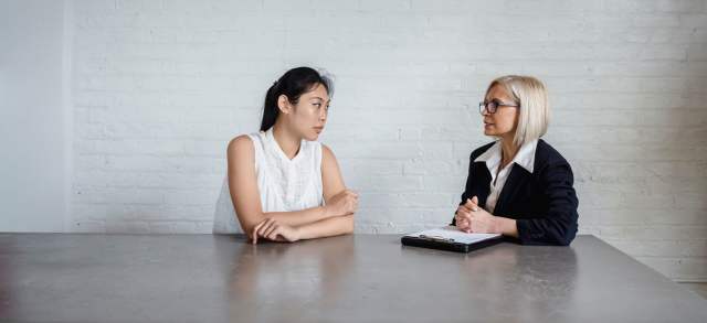 Bewerberin und Personalerin sitzen sich am Tisch gegenüber und führen ein Vorstellungsgespräch.