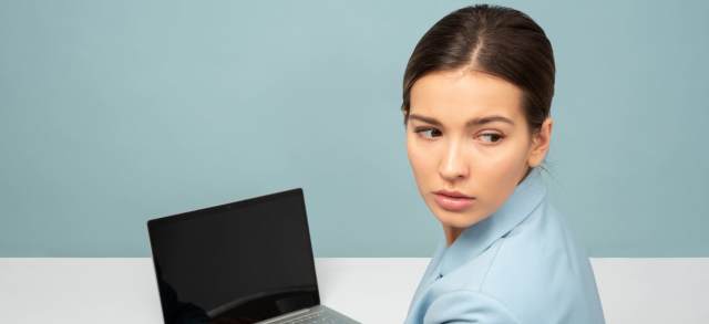 Junge Frau blickt am Laptop nachdenklich zur Seite und überlegt, welches duale Studium zu ihr passt.