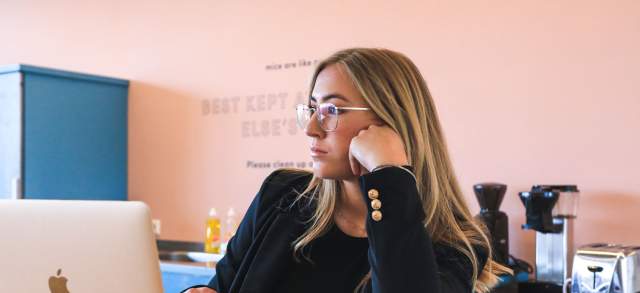 Eine Studentin mit Brille blickt nachdenklich auf ihren Laptop und wartet auf die Beurteilung ihres Studienerfolges.