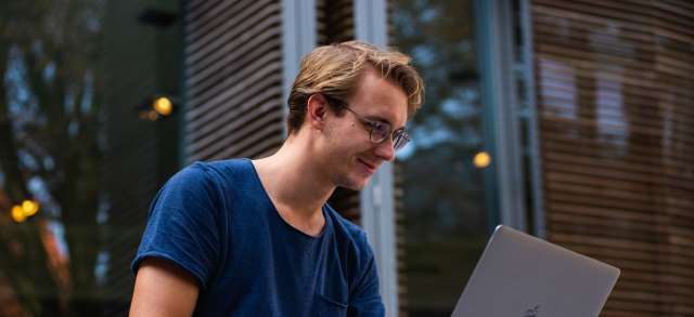 Ein junger Mann sitzt mit seinem Laptop draußen und informiert sich über das Studieren ohne Matura.