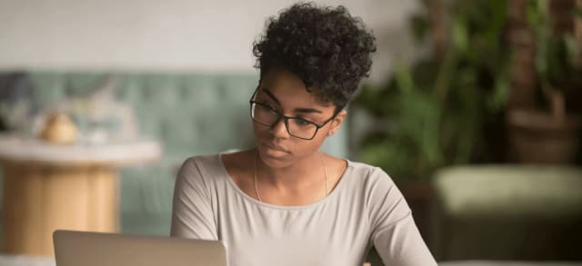 Woman with curly hair holding book and working on laptop