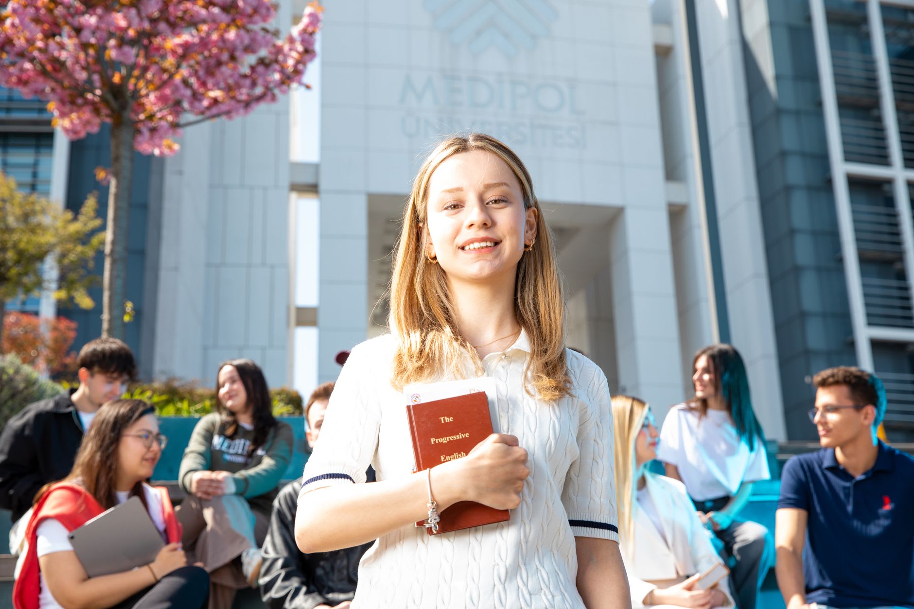 Eine Studentin steht mit einem Buch im Arm auf dem Campus einer ausländischen Universität.