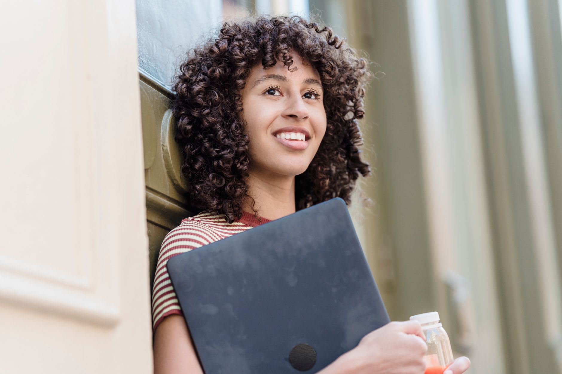Eine lächelnde junge Frau hält ihren Laptop im Arm und freut sich darauf, Psychologie im Ausland zu studieren.