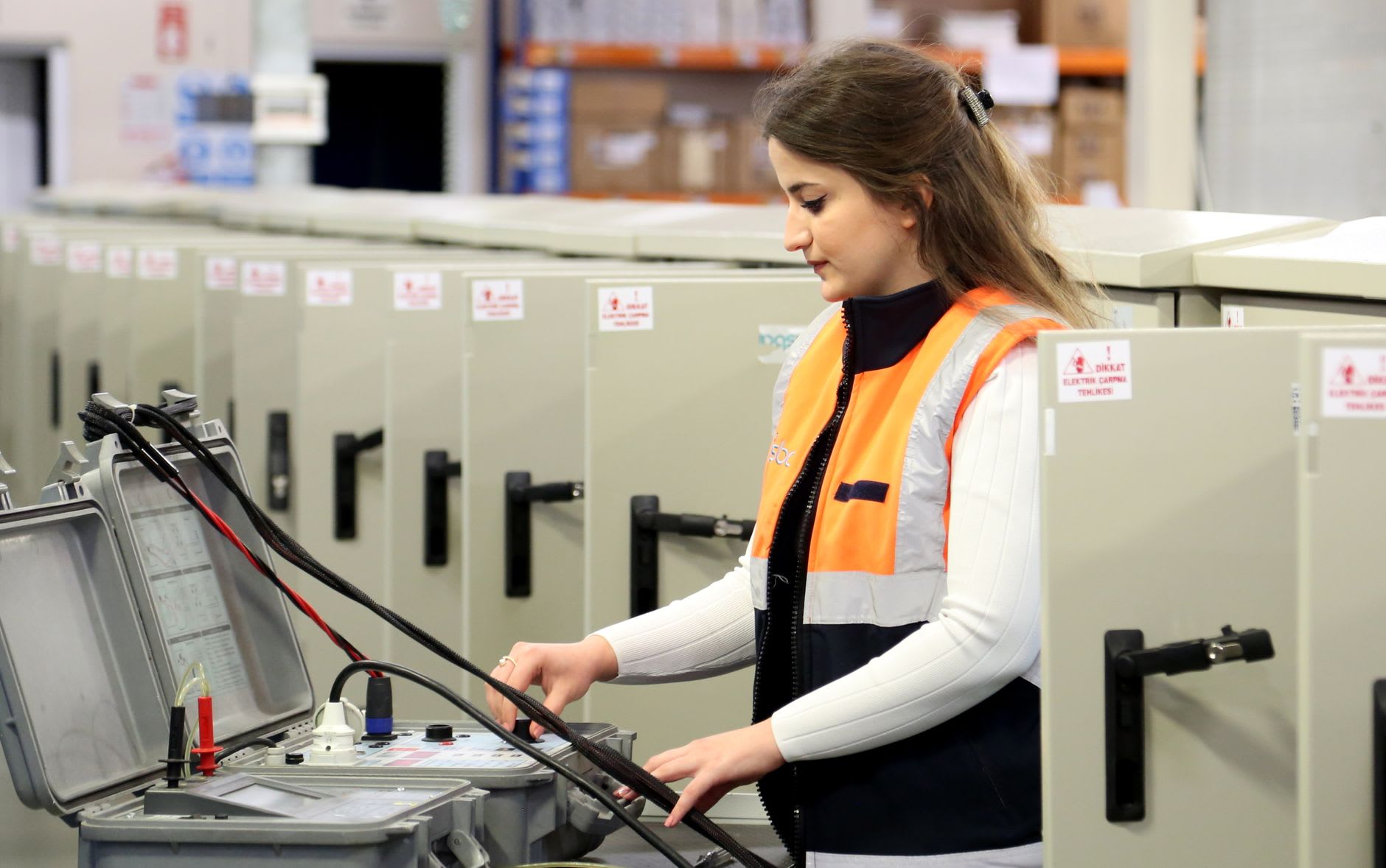 Elektrotechnikerin in Warnweste bedient ein Prüfgerät vor Schaltschränken.