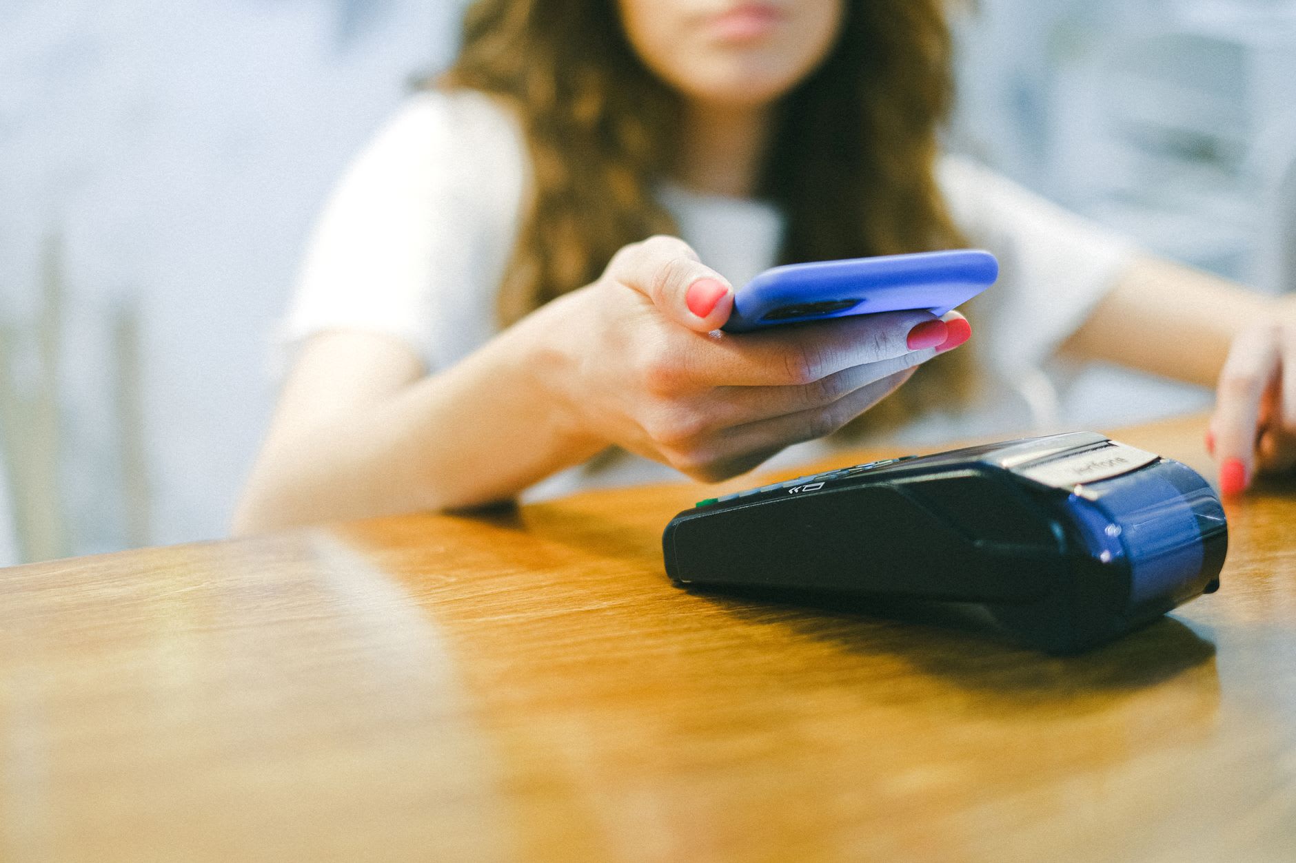 Eine junge Frau bezahlt kontaktlos mit dem Smartphone und denkt dabei an ihre Studienfinanzierung.