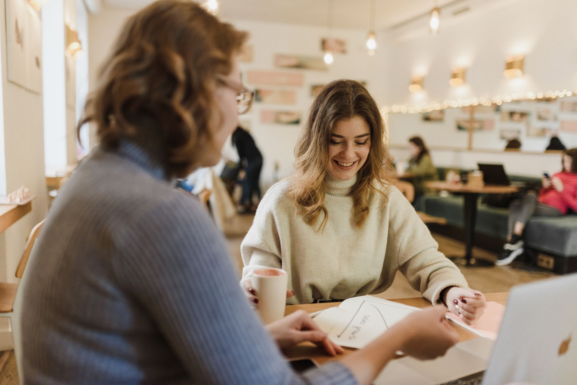 Zwei junge Frauen sitzen im Café zusammen und besprechen die Möglichkeiten eines Studienkredits.