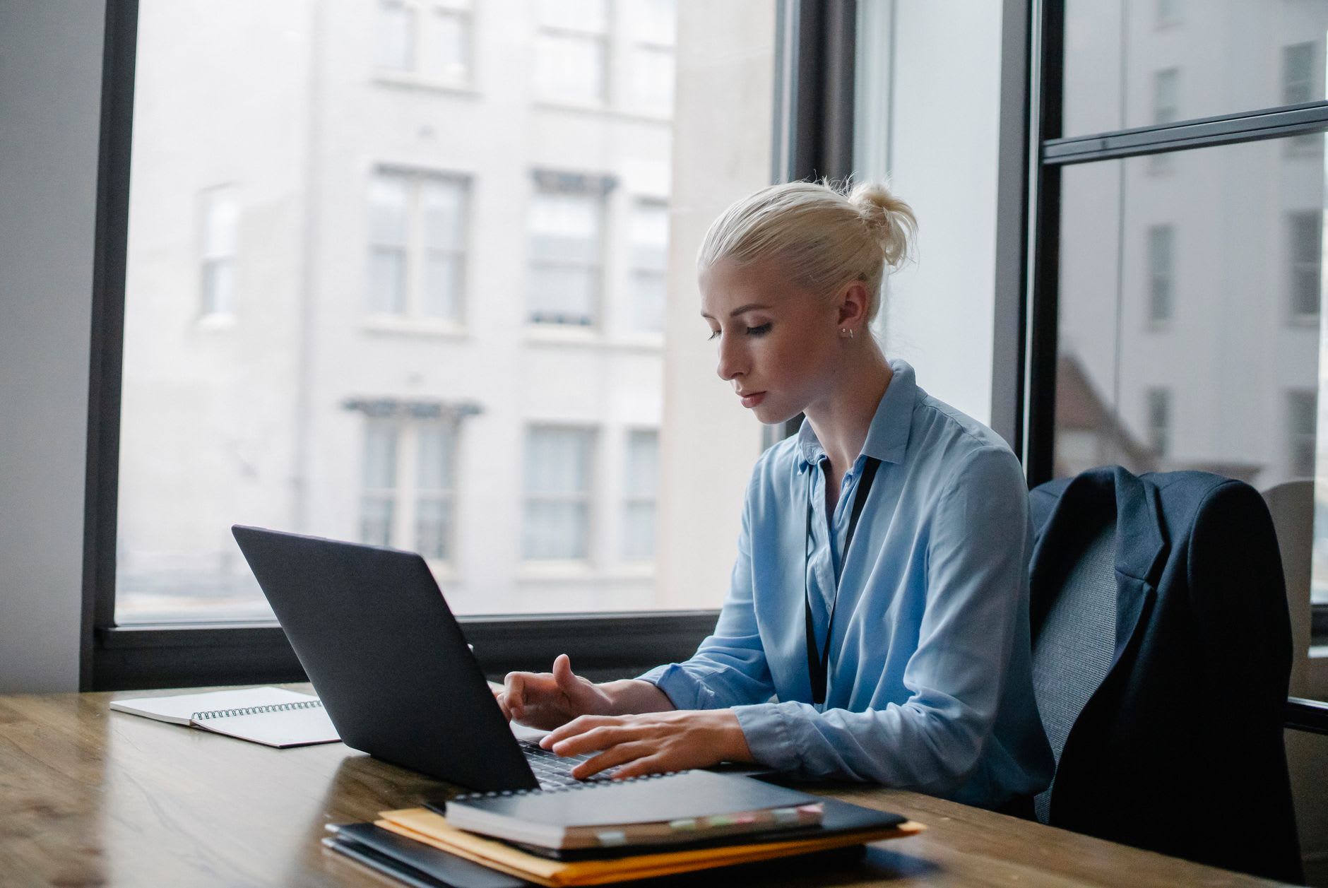 Eine junge Frau arbeitet konzentriert am Laptop im Büro und verbindet so Studieren und Arbeiten.