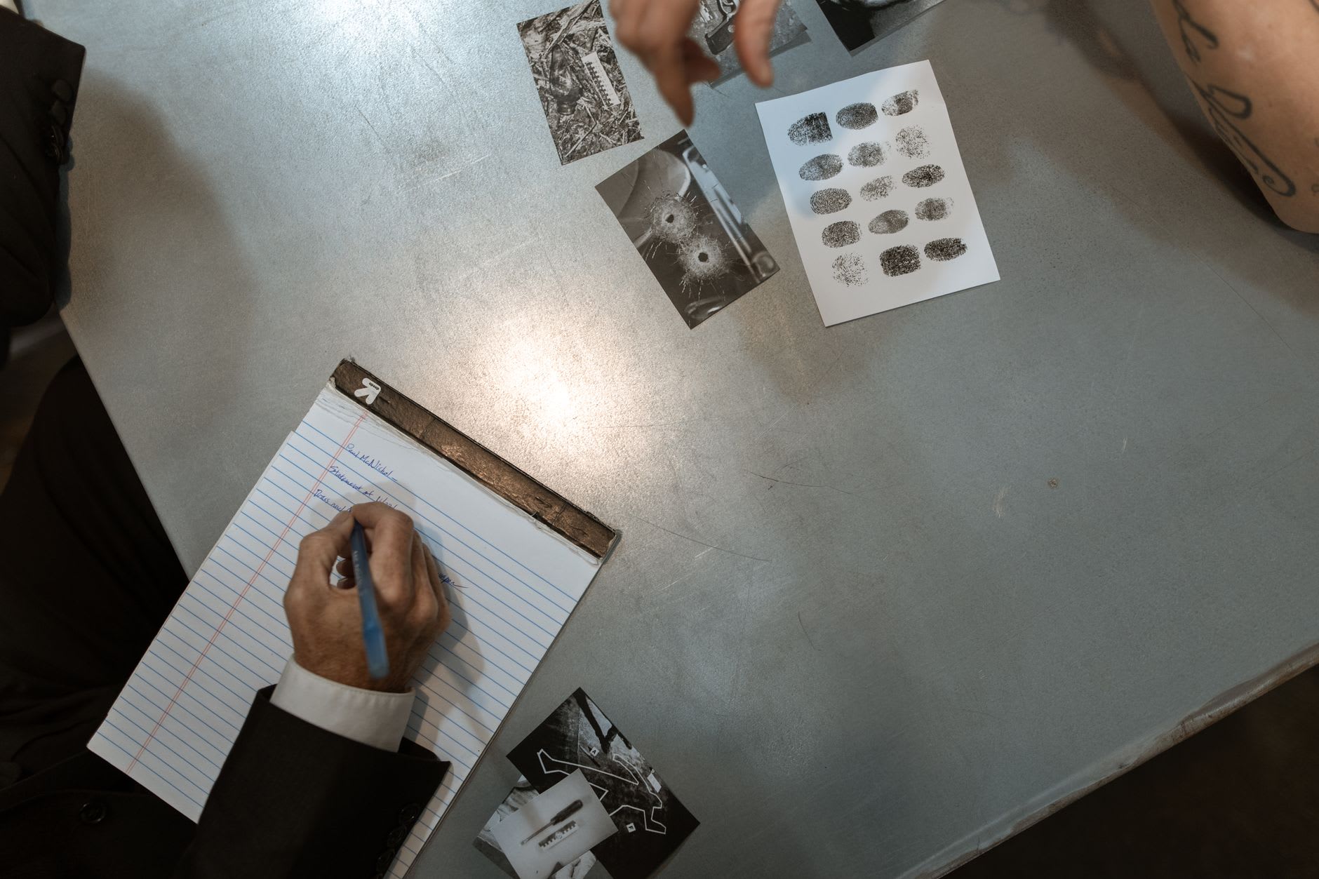 Ermittler notiert Beobachtungen neben Tatortfotos und Fingerabdrücken auf dem Tisch.