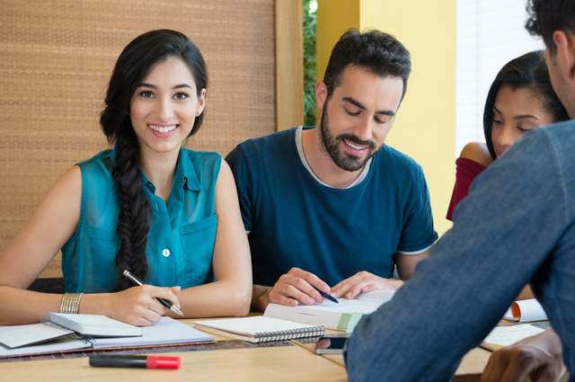 Closeup of young woman looking at camera while studying with her friends at library. Portrait of female student preparing for the exam.Beautiful young woman looking at camera.