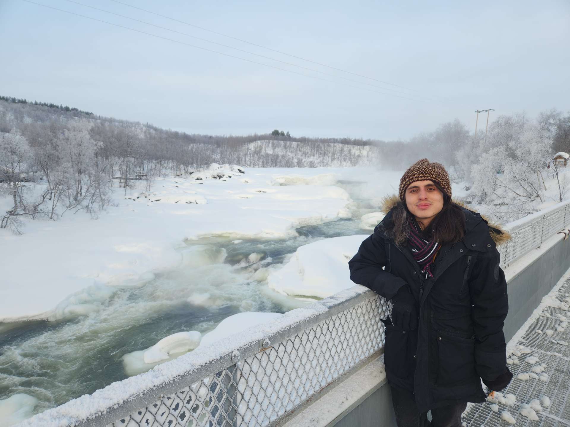 Nicolás in a winter wonderland, standing on a bridge with rapids flowing