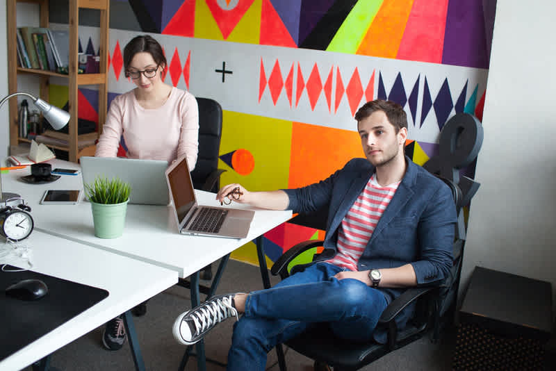 Young male in glasses discussing business with woman in modern office with laptops