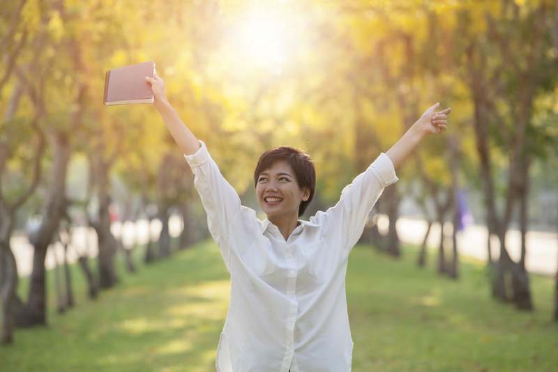 hapiness face of yonger woman and student book in hand standing in summer park