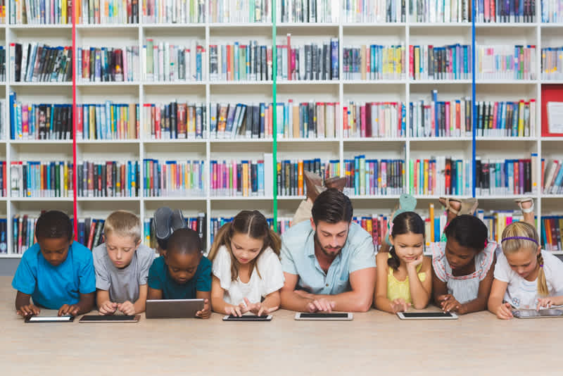 Teacher and kids lying on floor using digital tablet