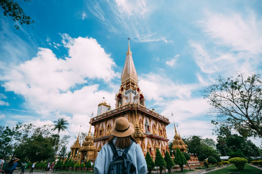Young woman traveler with backpack traveling into beautiful pagoda in Wat Chalong or Chalong temple at Phuket town, Thailand. It's most popular thai temple in Phuket Thailand.