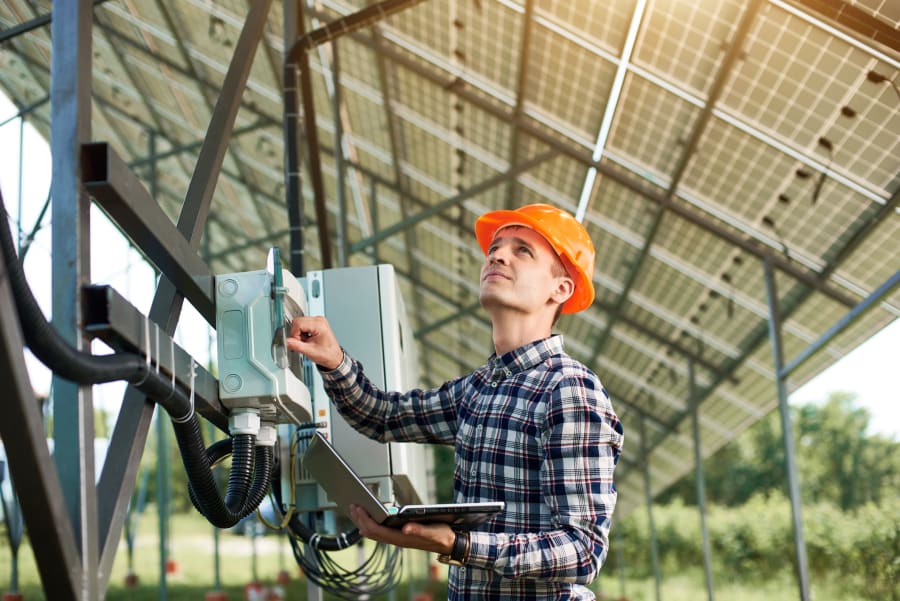 Operator in helmet and with laptop at station checking the operation of solar power plant.