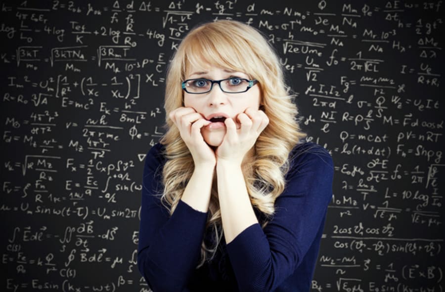 Closeup portrait nervous, stressed woman, nerdy scared student with eyeglasses biting fingernails looking anxiously, afraid of finals, isolated chalkboard background filled with math, physics formulas