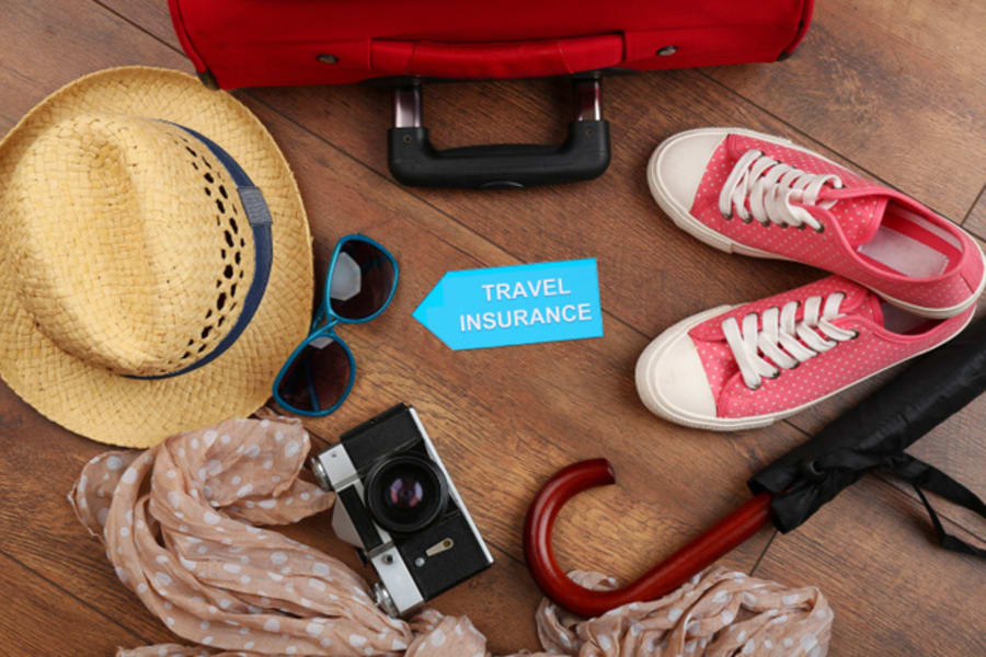 Suitcase and tourist stuff with inscription travel insurance on wooden background