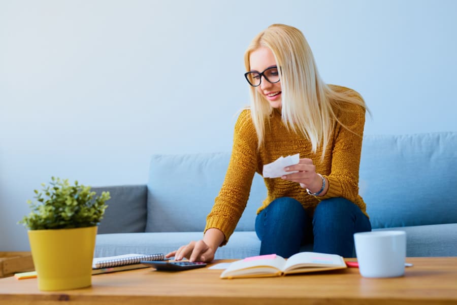 Young woman with bills calculating finances, sitting on sofa