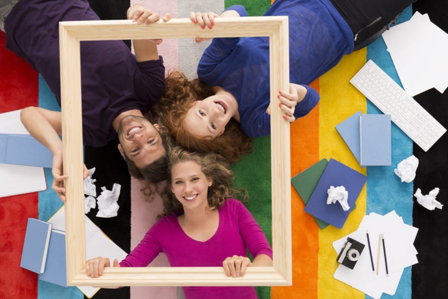 Top view of a happy three students holding a frame, colorful background