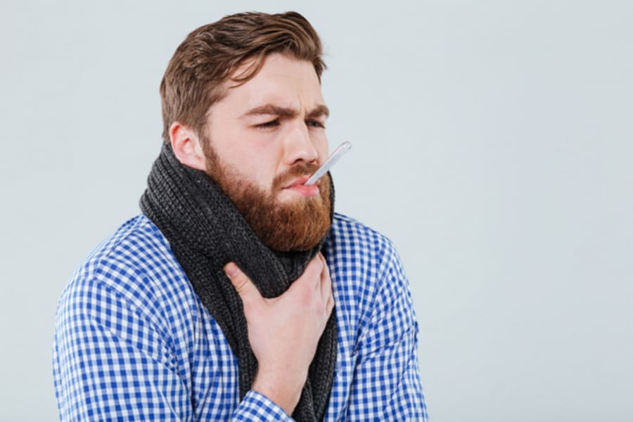 Man in scarf holding thermometer in his mouth measuring temperature