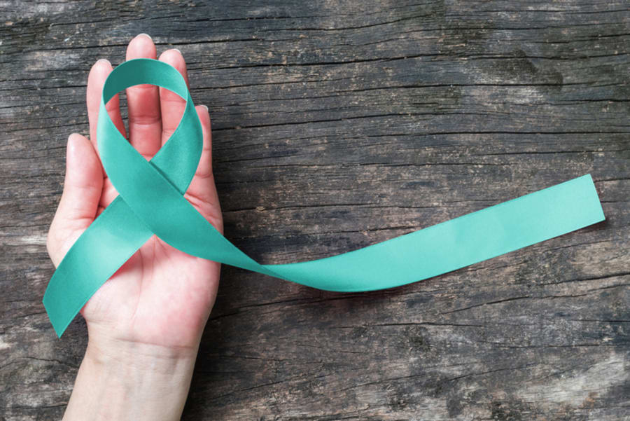 Teal ribbon awareness to support Ovarian/Cervical Cancer on human hand old aged wood background: Satin silk ribbon symbolic concept for raising concerns/ help and campaign on people living with illness, PTSD