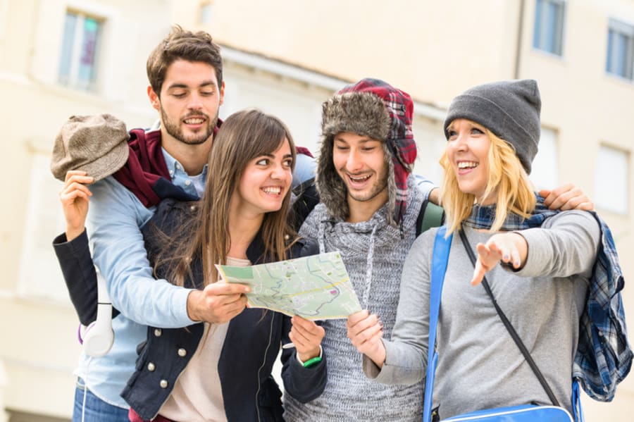 Group of young hipster tourists friends cheering with city map in the old town - Travel lifestyle concept with happy people having fun together - Winter fashion clothing wears with neutral color tones