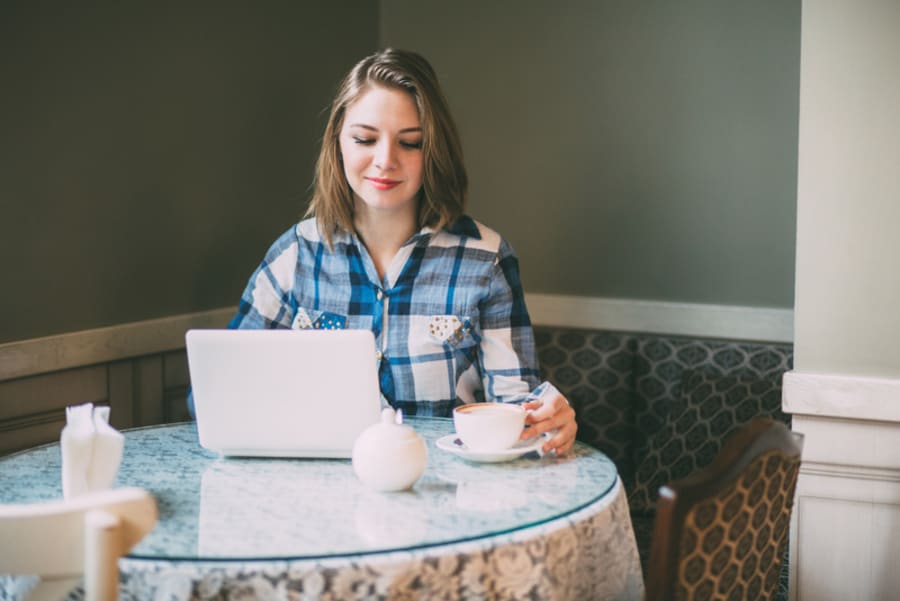 Young attractive businesswoman in plaid shirt wiorking with laptop in cafe.