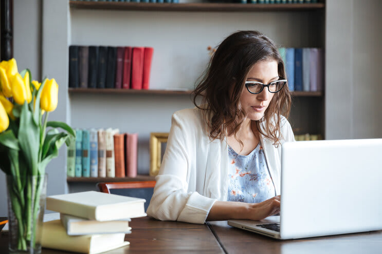 Potret seorang wanita bisnis dewasa yang berkonsentrasi mengerjakan laptop sambil duduk di meja di rumah