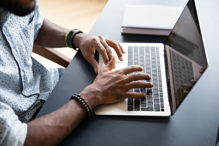 Zblízka pohled shora na afroamerického mladého muže, který píše textové zprávy na moderní klávesnici notebooku, biracální mužský zaměstnanec sedí u stolu a pracuje na počítači, konzultuje s klientem nebo studuje online, technologický koncept