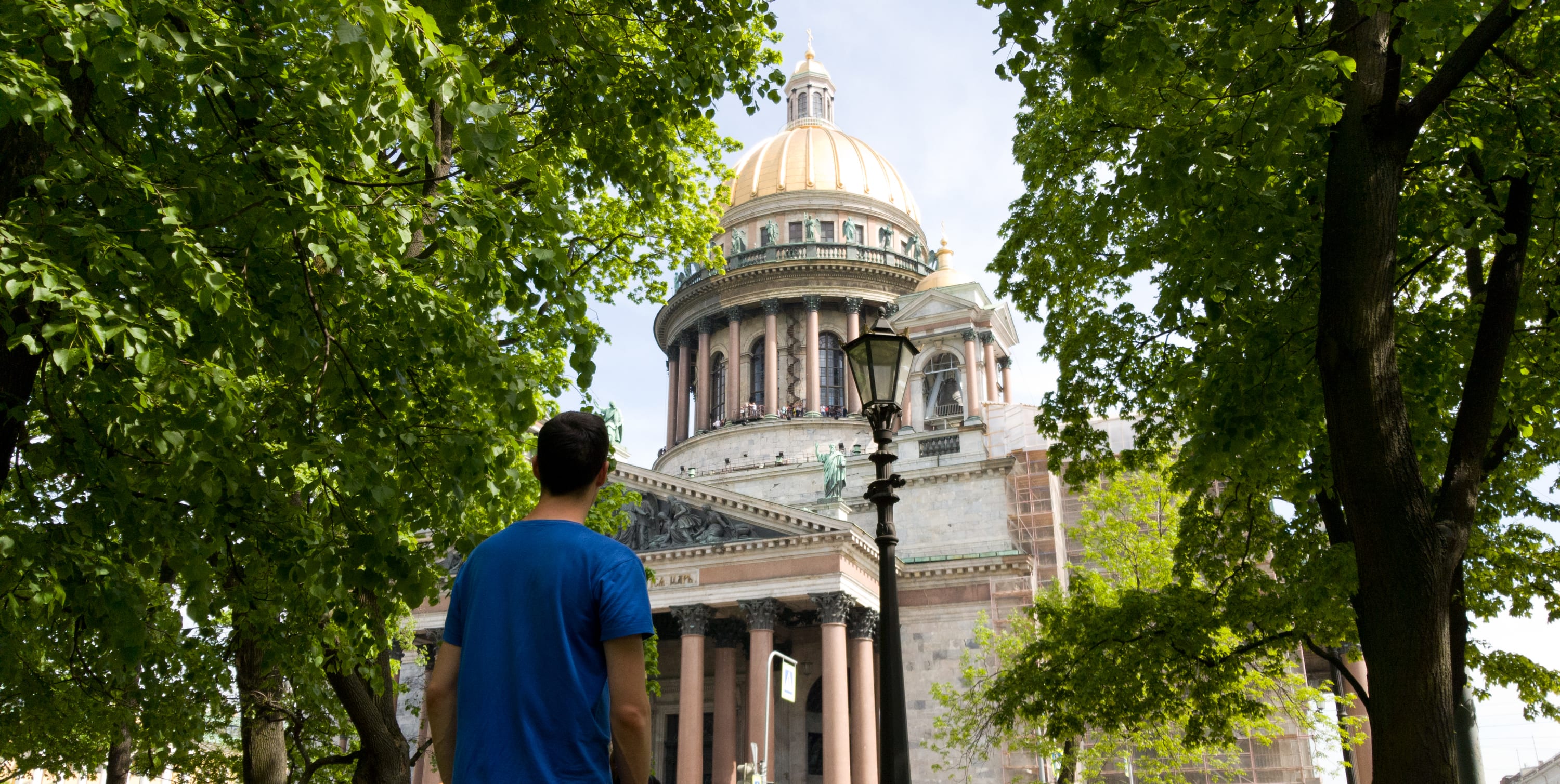 Beautiful view of St. Isaac's Cathedral in St. Petersburg. Lush foliage of trees. A male tourist admires the attraction. Summer trip to Russia