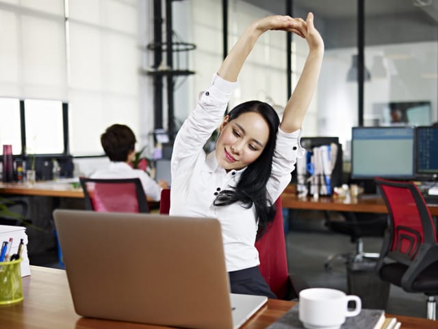 asian businesswoman looking at work on laptop computer with satisfaction and stretching arms in the air.