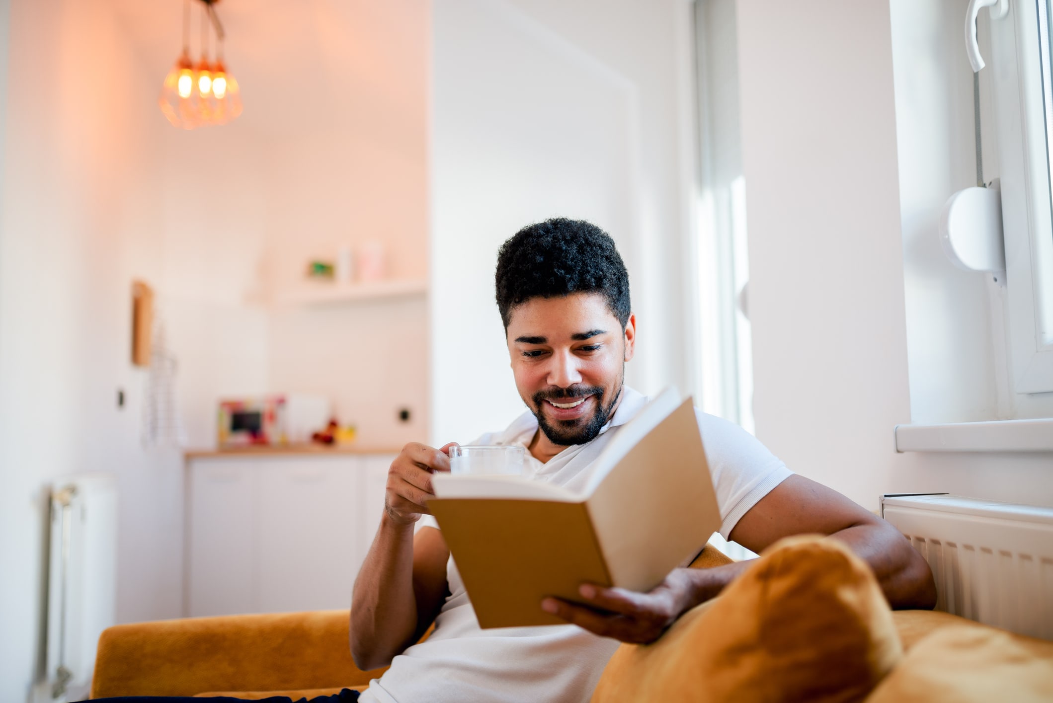 Handsome smiling man reading a book while sitting on the sofa.
