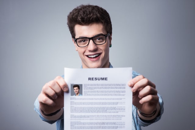 Young smiling man holding his resume applying for a job