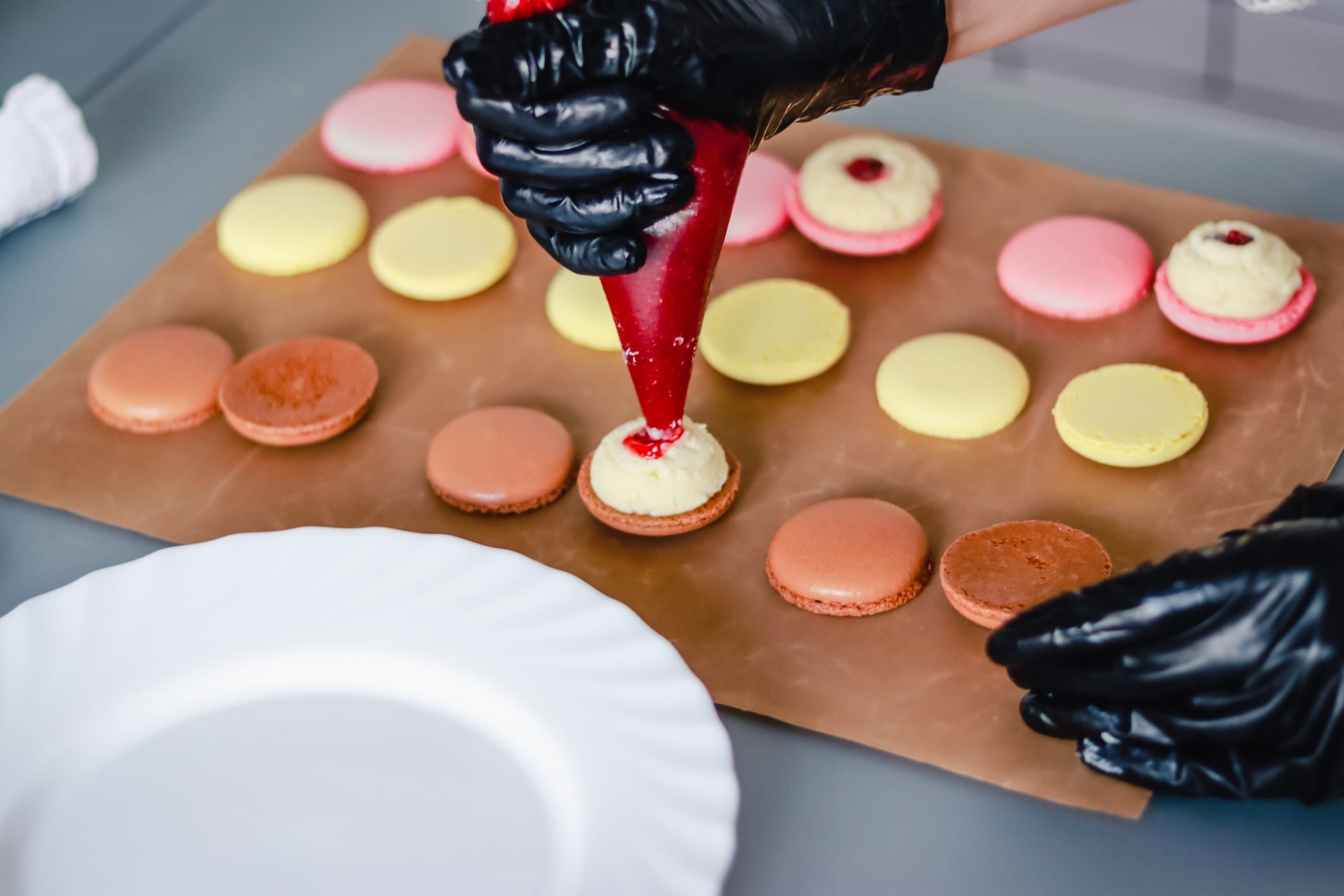 Confectioner in black rubber gloves stuffs macaroon cakes with jam