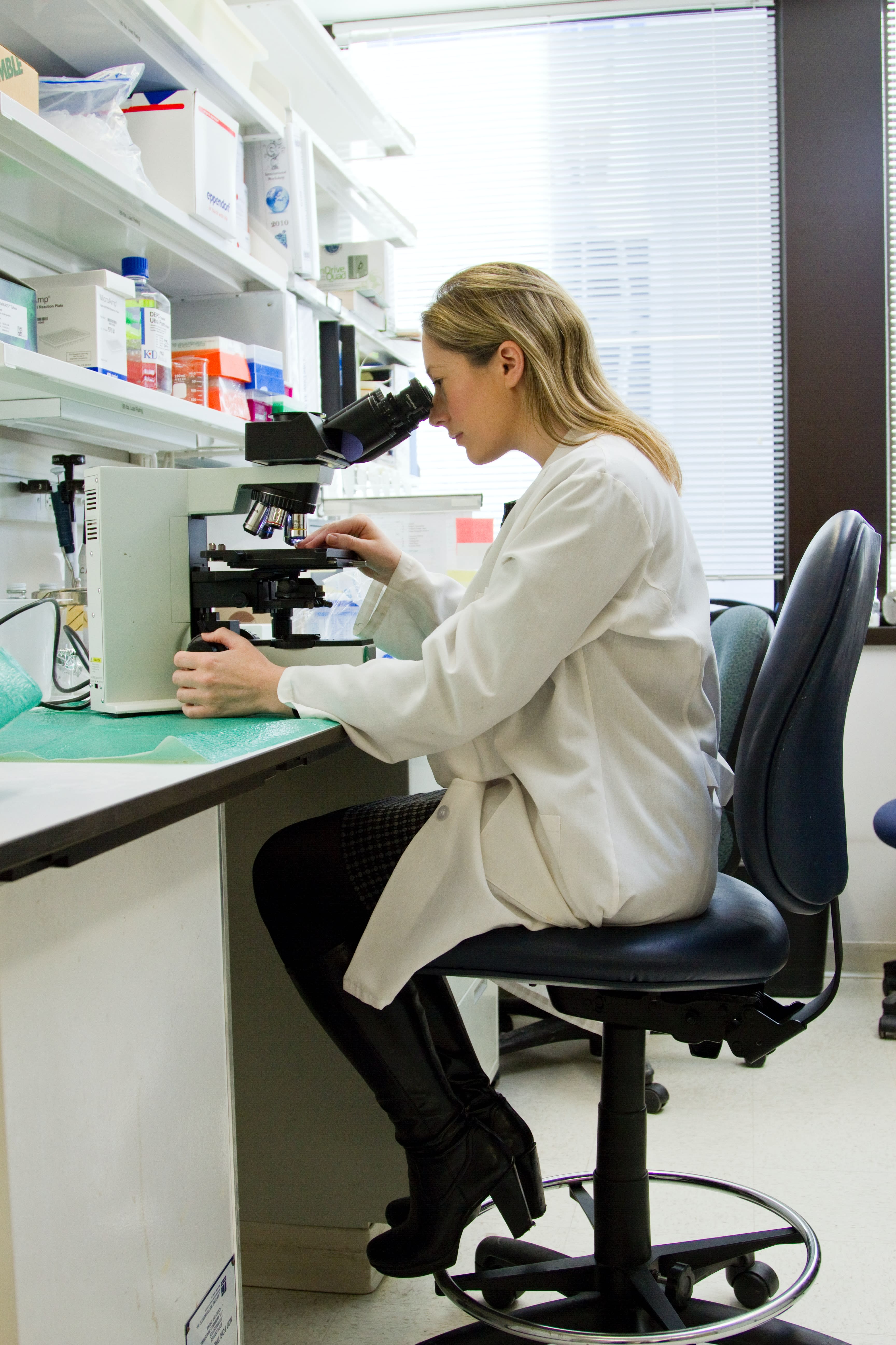Una scienziata in un laboratorio guarda attraverso un microscopio.