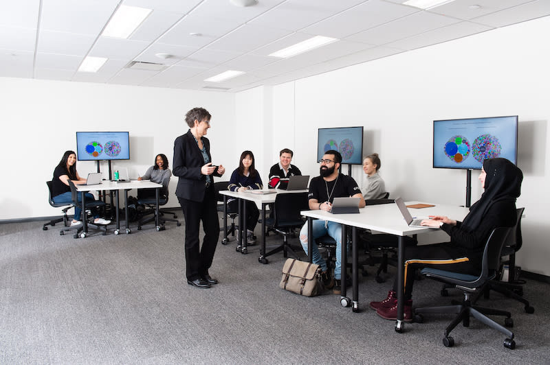 Insegnante in piedi in un'aula hi-tech, con studenti ai tavoli con schermi di computer