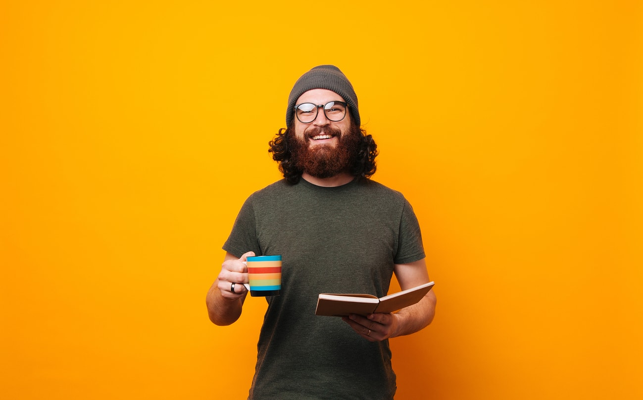 Happy man with coffee and book looking confident at the camera