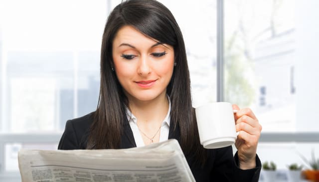 Beautiful woman reading the newspaper while drinking coffee
