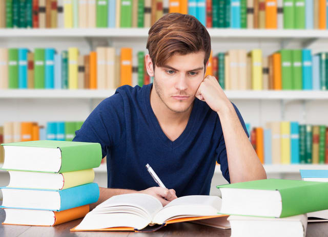 Serious Male Student Surrounded With Stack Of Books