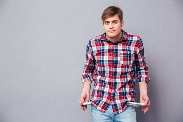 Poor handsome young man in checkered shirt showing empty pockets