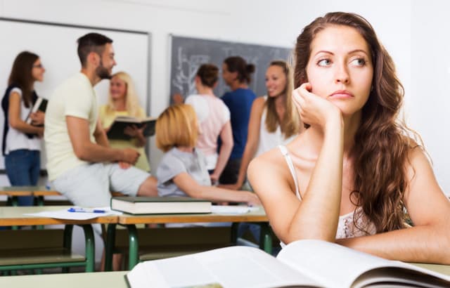 Dejected lonely student with sad expression sits at her desk in the classroom