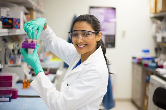 Closeup portrait, young scientist in white labcoat and goggles doing experiments in lab, academic sector.