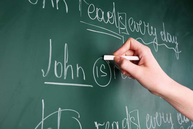 Teacher hand writing grammar sentences on blackboard background